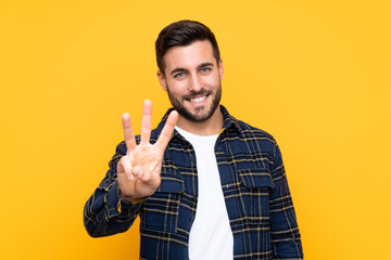 Poster - Young handsome man with beard over isolated yellow background happy and counting three with fingers