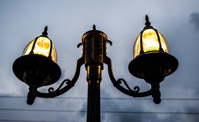 Beautiful lighted vintage lamp post at night with a cloudy sky in background