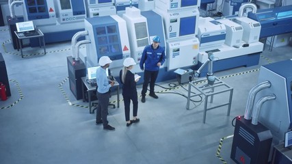 Fototapete - Industry Four Factory: Female Executive and Chief Engineer Inspect Facility Workshop, Look at robot arm working on Assembly Line, Talk to Worker. High-End CNC Machinery and Equipment. High Angle