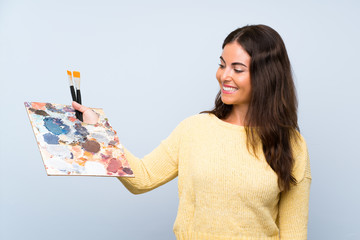 Wall Mural - Young artist woman over isolated blue background with happy expression