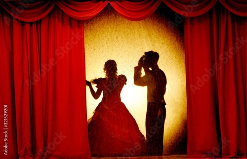 A man and woman in theatrical costumes in the theater of shadows on the stage with red curtains. Love in the shadows theatre. Red curtain of opera, cinema or theater stage drapes.