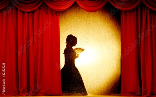 A man and woman in theatrical costumes in the theater of shadows on the stage with red curtains. Love in the shadows theatre. Red curtain of opera, cinema or theater stage drapes.