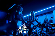 Smiling Twin Sisters Exercising On Spinning Bikes In Gym