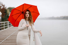 Portrait Of Young Woman With Red Umbrella, Leaning On Railing During Rainy Day