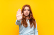 © luismolinero - Teenager redhead girl over isolated yellow background making stop gesture