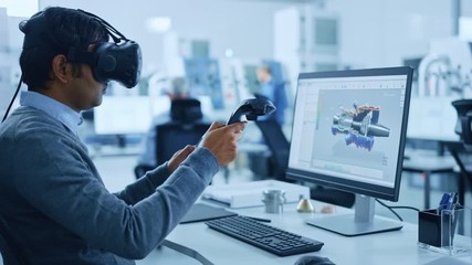Modern Industrial Factory: Mechanical Engineer Wearing Virtual Reality Headset, Holding Controllers, Uses VR technology for Industrial Design, Development and Prototyping in CAD Software on Computer.