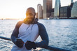© BullRun - Cheerful athletic black male in earphones browsing smartphone on urban background