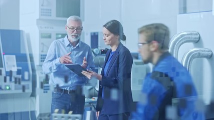 Wall Mural - Modern Factory: Female Engineer, Male Project Manager Standing in High Tech Development Facility, Talking and Using Tablet Computer. Contemporary Facility with CNC Machinery, Robot Arm Production Line