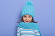 © sementsova321 - Close up portrait of little girl withastonish facial expression, wearing stripes shirt, cap and scarf, looking at camera, posing isoalted over purple studio background, sees something surprising.
