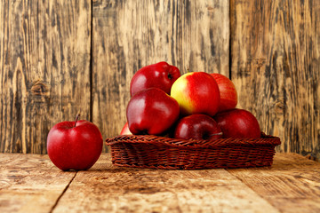 Wall Mural - Red ripe apples lie in a wicker basket on an old wooden table.