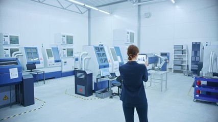 Wall Mural - Modern Factory: Female Engineer Uses Digital Tablet Computer with Augmented Reality Software to Visualize Workshop for Room Mapping, Floor Layout. Facility with High-Tech CNC Machinery and Robot Arm