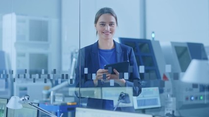 Poster - Modern Factory Office: Portrait of Young and Confident Female Industrial Engineer Standing and Holding Digital Tablet, She Smiles Charmingly at Camera. Industrial Factory with CNC Machinery Workshop