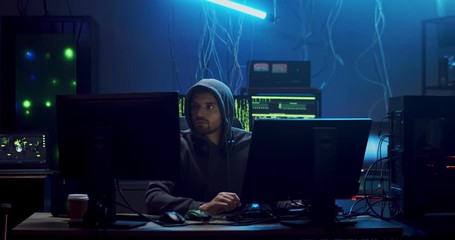 Caucasian young man hacker commiting cybercrime while hacking at two computers in the dark programming room with technologies.
