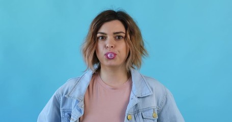 Wall Mural - Portrait happy smile woman in star sunglasses inflates bubble from chewing gum balloon and bursts it in on blue background. Slow motion. Emotions of people. Lifestyle. Party. Monotone. 