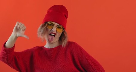 Wall Mural - Portrait of young sexy girl in red hat, red sweater listens to music, shows finger down with displeased face on red background looks directly at camera. Pleasure. Emotions of people. Monotone