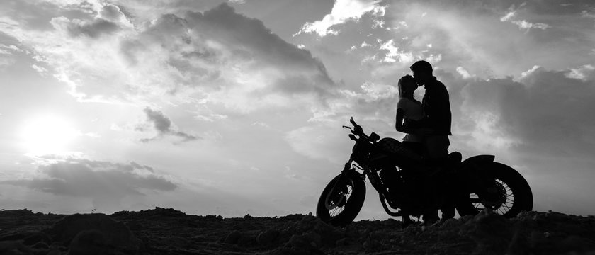 Fototapete - Silhouettes of a couple in love with a motorcycle on the background of the sunset sky