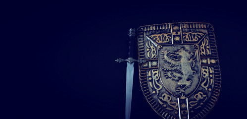 photo of shield knight armor and sword over dark background. Medieval period concept