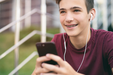 Close-up portrait of a smiling young man with a smartphone, in the street.  Happy teenage boy is using mobile phone, outdoors. Cheerful teenager spends time in social networks using cell phone.