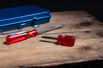 Two screw drivers and a tool box on a wooden surface