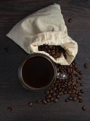 Wall Mural - glass mug with fresh black natural coffee, a bag with coffee grains and sprinkled grains of roasted coffee on a wooden table