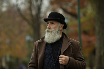 Fashionable senior man with gray hair and beard is outdoors on the street.