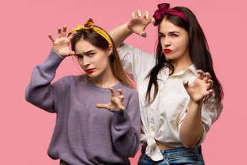 Isolated image of two emotional angry young Caucasian women frowning and holding hands as if going to attack, scare or intimidate you. Human facial expressions, emotions, feelings and body language