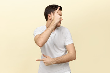 Wall Mural - Portrait if active energetic young man having fun making gestures as if holding pistol. Handsome dark haired guy dancing against white blank studio wall background with copy space for your information