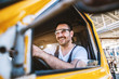 © dusanpetkovic1 - Smiling handsome unshaven worker driving vehicle on construction site.