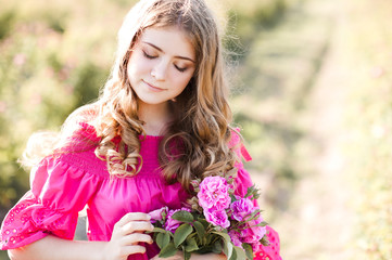 Canvas Print - Smiling teen girl 16-17 year old with blonde long curly hair holding fresh pink roses posing in meadow outdoors in sunny day. Spring time season.