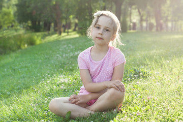 beautiful little girl in pink t-shirt on grass. tired girl after walk in the city park