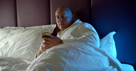 man is answering on sms and calling by mobile phone lying in bed in night time