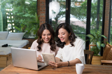 Two freelancer Asian colleagues using laptop computer at cafe table