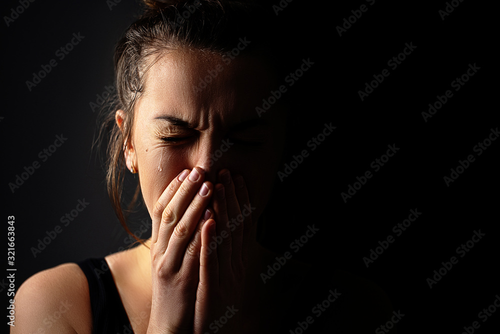 Sad grieving crying female with folded hands and tears eyes on a dark black background during trouble, life difficulties, loss and emotional problems. Copy space - obrazy, fototapety, plakaty 