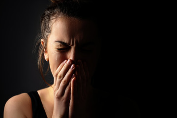 Wall Mural - Sad grieving crying female with folded hands and tears eyes on a dark black background during trouble, life difficulties, loss and emotional problems. Copy space