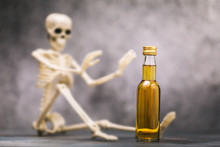 Human Skeleton And A Bottle Of Whiskey On The Table. Concept On The Harm Of Alcohol To Health