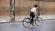 © alex_marina - A girl rides a bicycle along the road along the buildings. A girl in a black hat and suspenders
