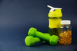 Plastic shaker, green dumbbells and a can of omega 3 on a blue background