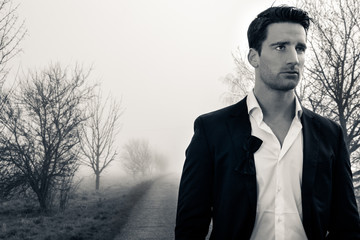 Handsome man wearing suit walking on a lonely foggy road