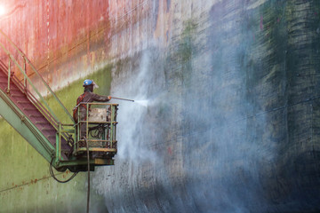 Man cleaning  the bottom of a sailboat with high pressure water at Cargo ship moored in dock yard on Retro tone.