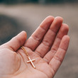 Eine Hand die ein goldenes Kreuz behutsam hält. Symbolisiert Vertrauen in Gott, Glaube, Kruzifix, Religion und Christentum.