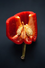 Red sweet pepper in the shape of a tulip flower. Close-up of cutting bell peppers with seeds and pulp on a black background. Organic food.