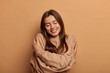 © wayhome.studio  - I love myself. Pretty smiling woman embraces herself gently, expresses self love, keeps eyes closed with pleasure, feels comfortable and fullfilled, being egoistic person, isolated on brown background