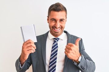 Wall Mural - Young handsome business man holding blank notebook over isolated background happy with big smile doing ok sign, thumb up with fingers, excellent sign