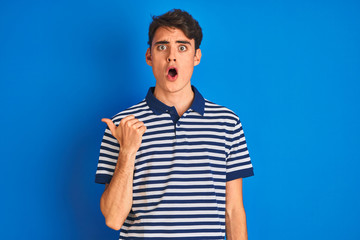 Sticker - Teenager boy wearing casual t-shirt standing over blue isolated background Surprised pointing with hand finger to the side, open mouth amazed expression.