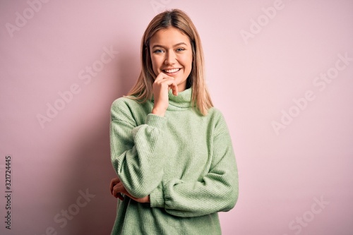 Young beautiful blonde woman wearing winter wool sweater over pink isolated background looking confident at the camera with smile with crossed arms and hand raised on chin Tableau sur Toile