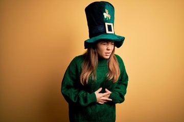 Canvas Print - Young beautiful brunette woman wearing green hat on st patricks day celebration with hand on stomach because nausea, painful disease feeling unwell. Ache concept.