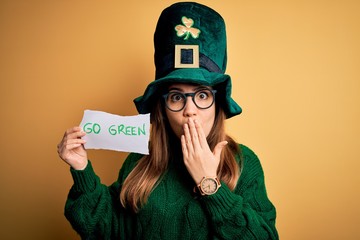 Sticker - Young beautiful woman wearing green hat and glasses on saint patricks day celebration cover mouth with hand shocked with shame for mistake, expression of fear, scared in silence, secret concept