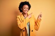 Young beautiful African American afro businesswoman with curly hair wearing yellow jacket smiling and looking at the camera pointing with two hands and fingers to the side.