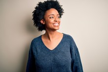Young Beautiful African American Afro Woman With Curly Hair Wearing Casual Sweater Looking Away To Side With Smile On Face, Natural Expression. Laughing Confident.