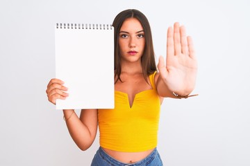 Wall Mural - Young beautiful student girl holding notebook standing over isolated white background with open hand doing stop sign with serious and confident expression, defense gesture